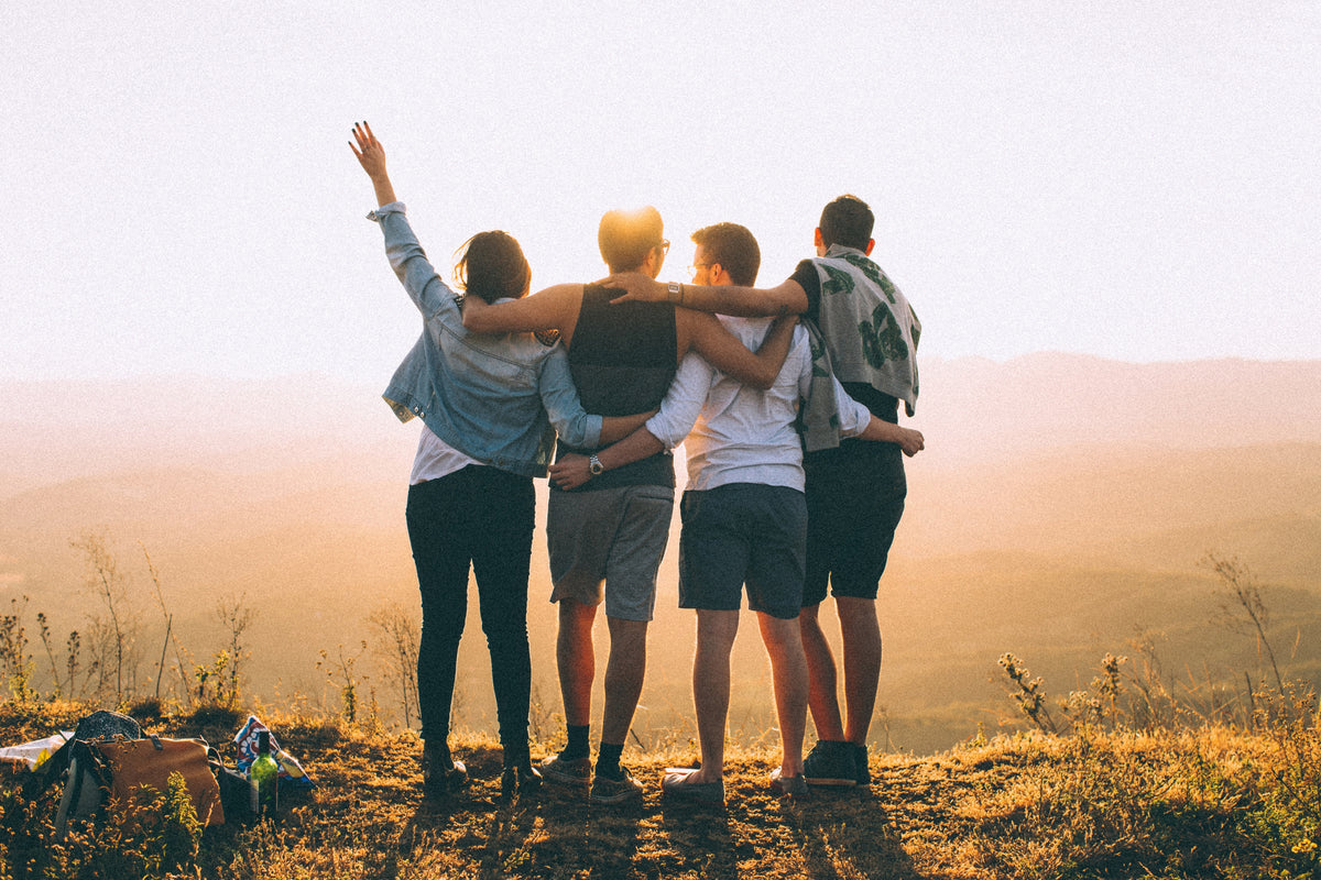 Four friends with arms around each other watching golden sunset