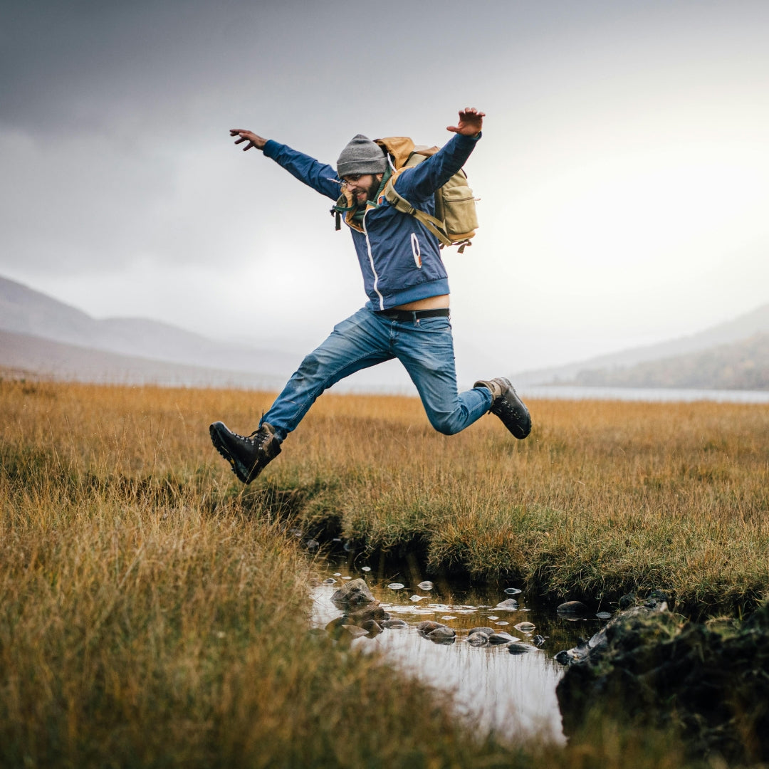 Active man wearing hiking gear jumping over small mountain puddle