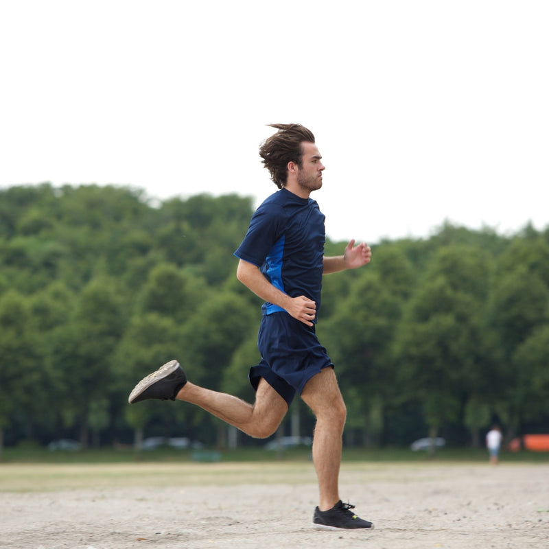Fit man in sportswear running across a dirt trail outdoors