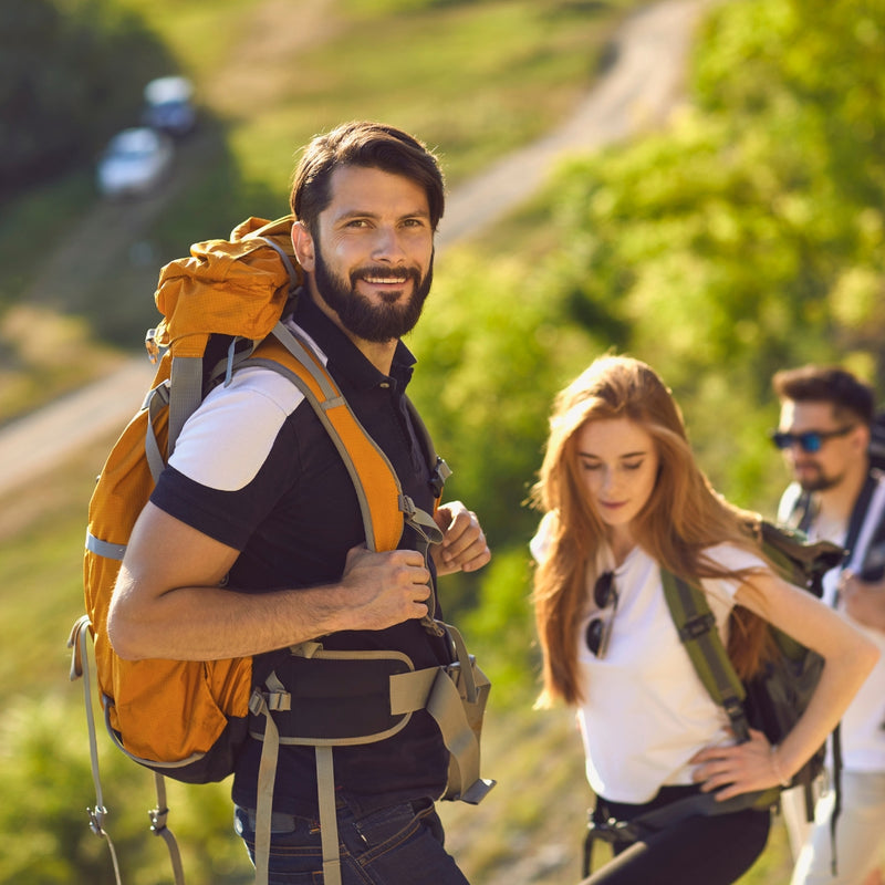 Group of three hikers with backpacks trekking up grassy mountain trail