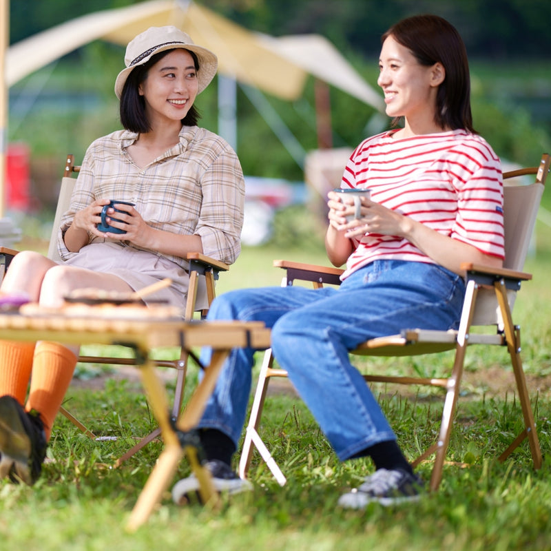 Two smiling women sitting in folding chairs at a campsite