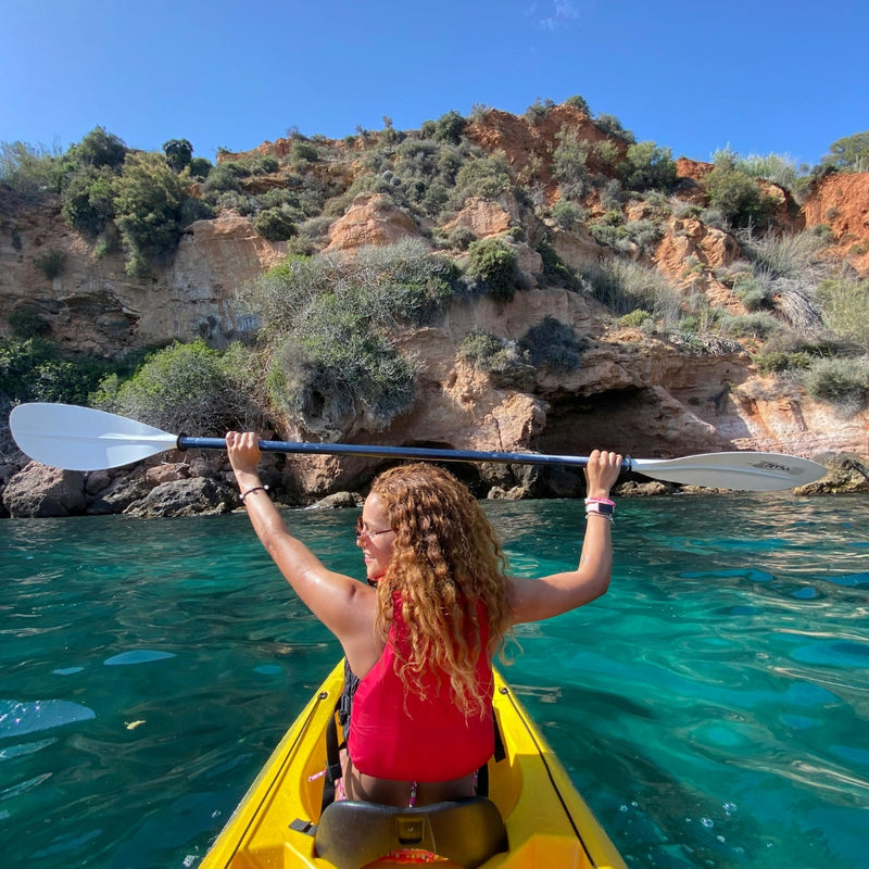 Woman kayaking in yellow boat near beautiful rocky mountain coast